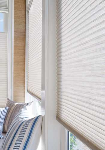 Window with white blinds and striped pillows on a bed