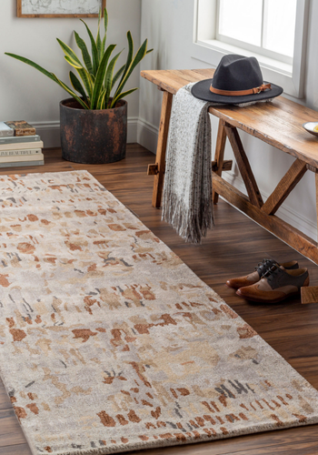 Patterned rug on a wooden floor with a wooden bench and plant in the background.2