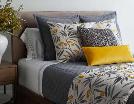 Decorative bed with patterned pillows and a yellow accent pillow, next to a wooden nightstand.