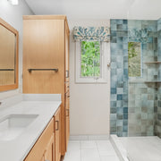 Bathroom with wooden vanity, mirror, and shower with teal blue tiles.