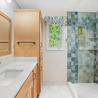 Bathroom with wooden vanity, mirror, and shower with teal blue tiles.