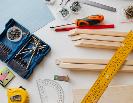 Tools and materials on a white surface including a ruler, wooden sticks, and a toolbox.